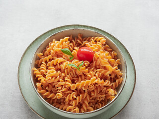 close-up view of red pasta spirals (fussili) dish with cherry tomatoes and fresh basil leaves on top