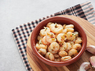 close-up view of fried shrimp with garlic and chili served in an earthenware casserole dish, with raw garlic heads on the side
