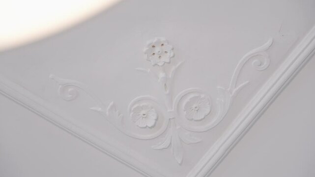 Close-up of ornate floral plasterwork on a white ceiling, showcasing intricate design details.