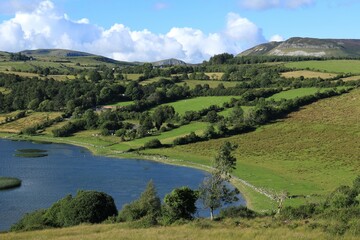 Landscape in rural County Sligo, Ireland featuring Lough Colgagh surrounded by hillside green fields of farmland pastures bordered by trees with mountains visible in 