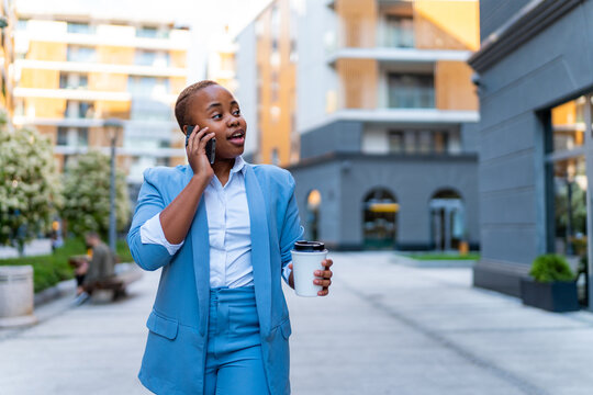 A young businesswoman walks to the office after a break with a coffee in her hand and talks on the phone