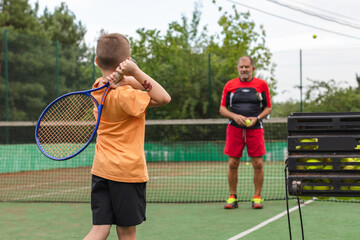 Tennis instructor assisting little boy on the tennis court.