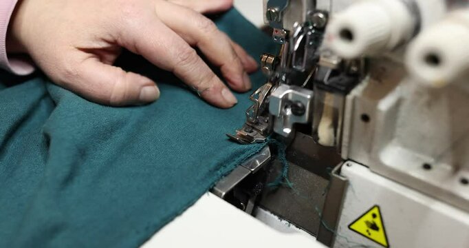 Employee expertly stitches textile using overstitching machine