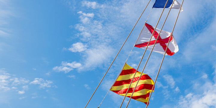 Diagonal hanging vibrant colorful nautical marine pattern signal system flags billowing on stretched cable lines with blue sky background