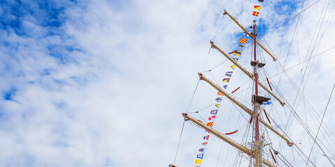 Sailing ship mast with flying nautical flags festival celebration decoration in a blue sunny sky and clouds, rigging of old tall ship with colorful bunting strung © gudzar
