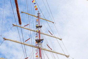 Sailing ship mast with flying nautical flags festival celebration decoration in a blue sunny sky and clouds, rigging of old tall ship with colorful bunting strung