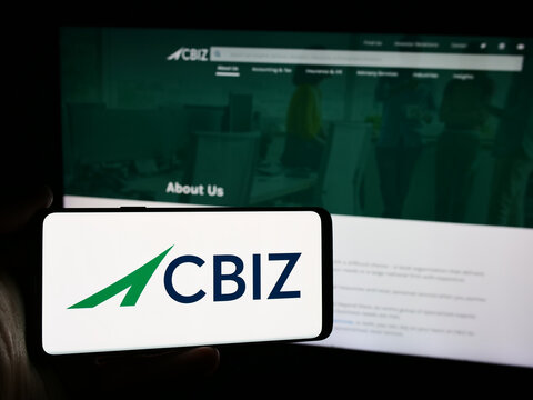 Stuttgart, Germany - 07-06-2024: Person holding mobile phone with logo of American financial consulting company CBIZ Inc. in front of business web page. Focus on phone display.