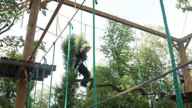Teenager child overcomes obstacles in the rope town. A girl with a helmet on her head and protective gear is on the track