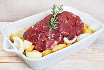 Raw all beef roast prepared with potatoes, onions and garlic in a white square dish ready for the oven