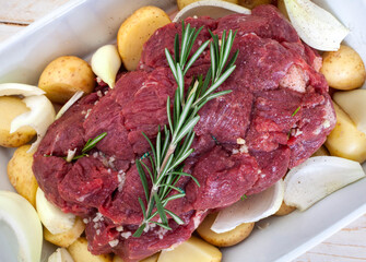 Raw all beef roast prepared with potatoes, onions and garlic in a white square dish ready for the oven