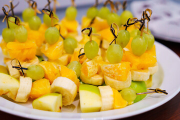 A plate with fruity canapes made from apples, bananas, oranges and grapes.