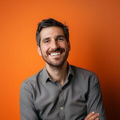 Fototapeta premium Smiling Man With Arms Crossed in Front of Orange Wall