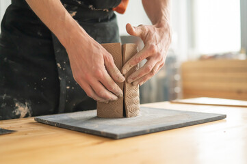 Close-up of a man's hands making a patterned cylinder out of clay. 