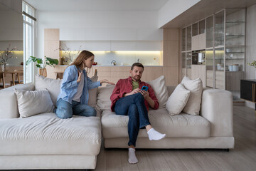 Cold man ignores angry woman making claims. Detached husband uses smartphone, gets stuck on social...