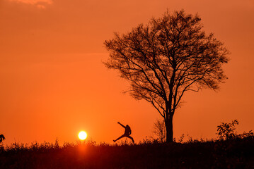 A silhouette of a man jumping with tree in the sunset.