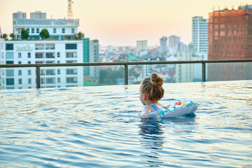 Naklejka premium A beautiful little girl swims in a pool with an inflatable circle on the roof of a skyscraper in Phnom Penh, Cambodia.