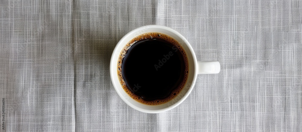 Poster a top down view of a hot cup of black coffee in a white mug on a gray tablecloth serving as a copy s