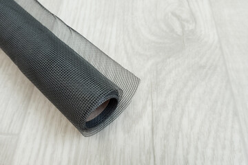 Black mosquito net in a roll close-up on a white wooden background.