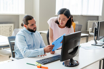 Attractive middle aged Arab ceo businessman holding documents, his beautiful Asian secretary talking
