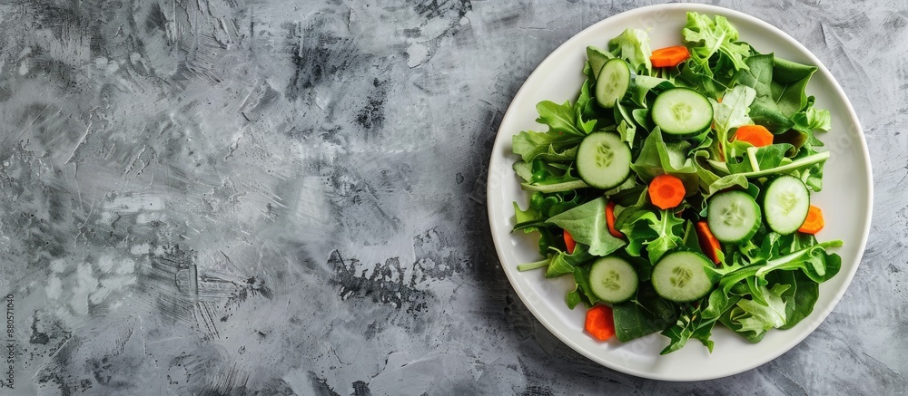 Poster Minimalist style photo of a green salad with cucumbers and carrots on a white plate against a grey backdrop with a horizontal orientation and space for text. copy space available