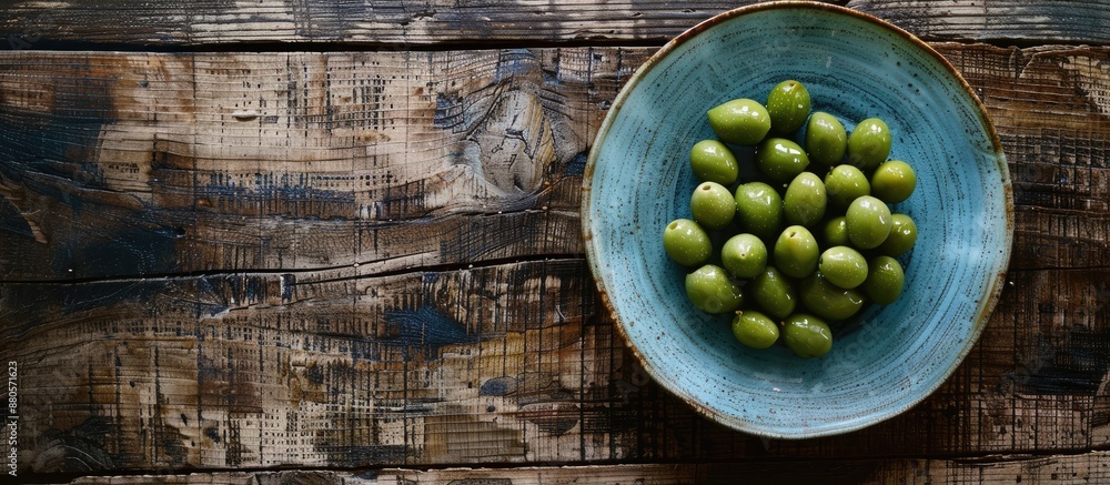 Poster Top view of a ceramic plate with green olives on a rustic wooden table with ample copy space image