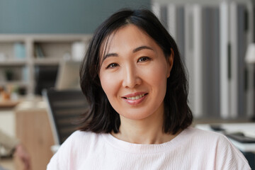Portrait of smiling, attractive Asian woman smiling posing in office looking at camera