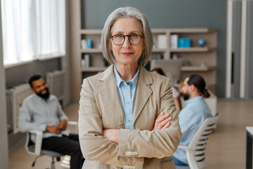 Obraz premium Confident senior businesswoman posing with arms crossed in modern office