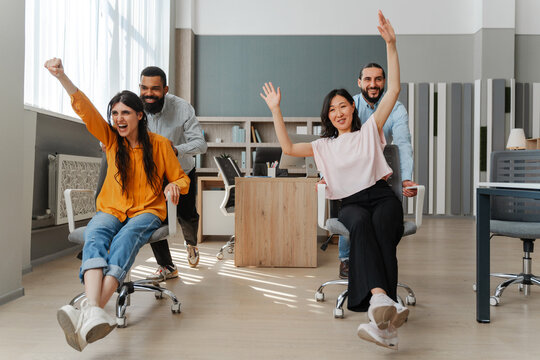 Happy multiethnic business team having fun racing on chairs in office