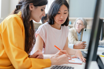 Two women collaborating on a project in busy office