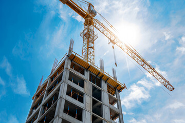 Waterrelled yellow crane and concrete building construction site against blue sky background