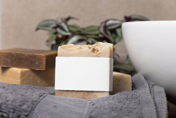 Soap bar with blank label near grey towels, plant and basin on wood in bathroom, mockup
