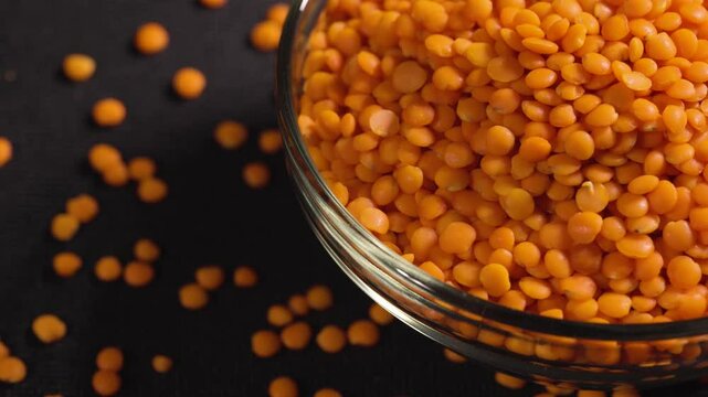 Red lentils in glass bowl. Dry orange lentil grains, heap of dal, raw daal, dhal, masoor, Lens culinaris or Lens esculenta on dark background
