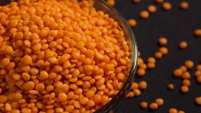Raw red lentils are scattered out of the glass bowl.