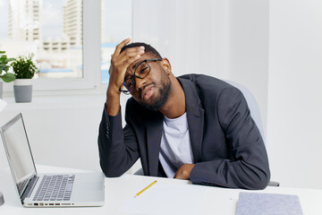 Stressed businessman in suit sitting at desk with head in hands and laptop, facing work or financial problems