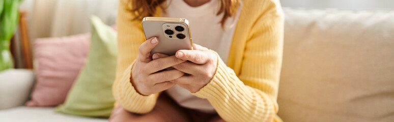 Middle aged woman sits on couch, engrossed in phone.