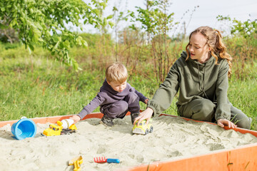 Babysitter and Kid Playing in Sandbox Together