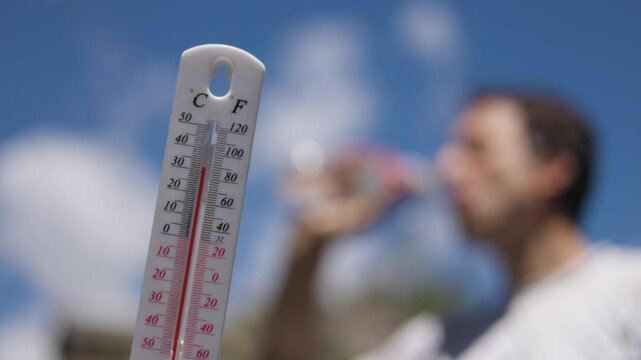 Man pouring water on his head in extreme heat. Thermometer in summer day shows or indicate high temperature degree with sun in background.
