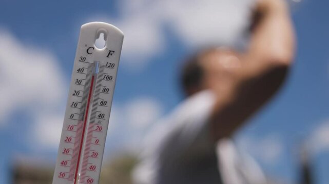 Man pouring water on his head in extreme heat. Thermometer in summer day shows or indicate high temperature degree with sun in background.