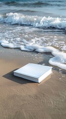 Closed white hardcover book is lying on wet sand with ocean waves crashing in the background, evoking a relaxing summer reading experience