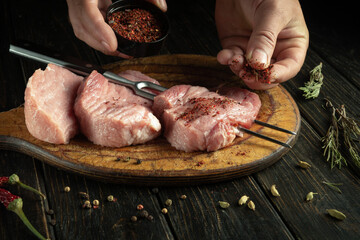 A butcher prepares steaks for grilling with spices by hand.