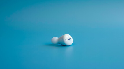 Single white wireless earbud lying on blue background