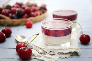 Cherry panna cotta in two glasses and fresh cherry on light surface