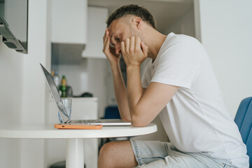 Obraz premium Young man experiencing burnout and stress while working on laptop at home, midlife crisis, mental health issues.