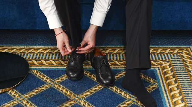 A man puts on black leather dress shoes. without a face. 