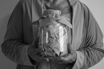 A person holds a glass jar filled with paper money