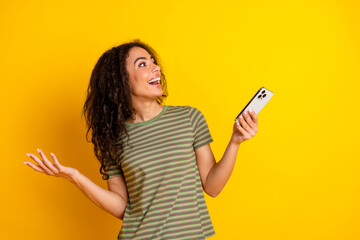 Photo of smart girl with wavy hairstyle dressed striped t-shirt hold smartphone look empty space isolated on yellow color background