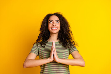 Obraz premium Photo of cheerful girl with wavy hair dressed striped t-shirt holding palms together look empty space isolated on yellow color background