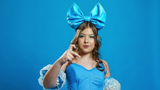 Cute teenage girl in blue doll costume singing, gestures on blue background. 