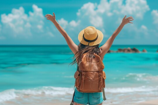 Happy woman with backpack standing with arms up at the beach