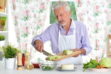 Happy retired senior man cooking in kitchen. 